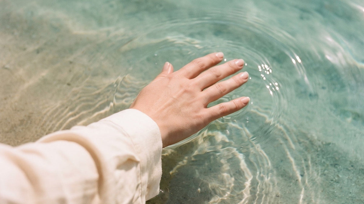 A hand trailing fingertips through clear turquoise water