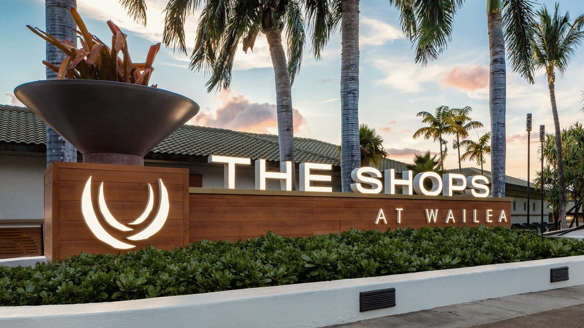 The Shops at Wailea entrance sign under palm trees at sunset