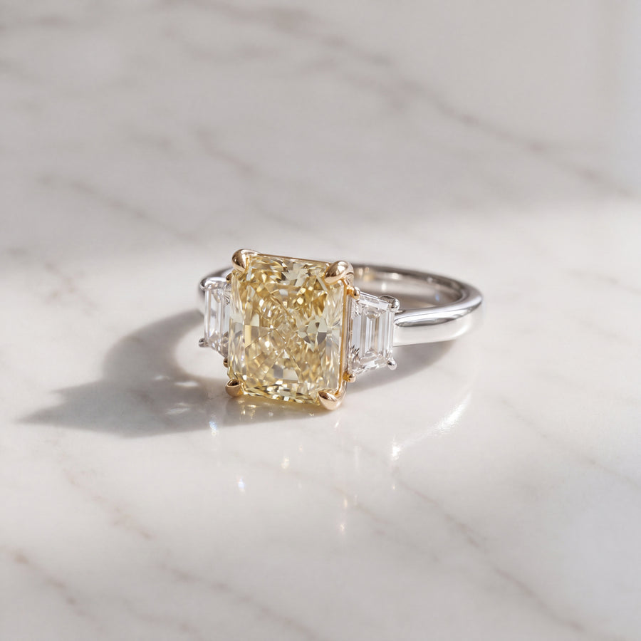 A near-square radiant-cut yellow diamond in yellow gold prongs between two colorless stones.