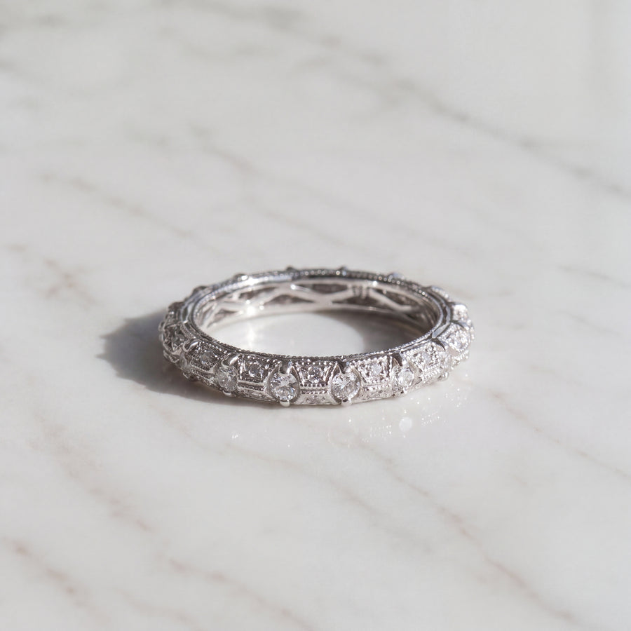 A white gold eternity ring of bead-set diamonds framed by intricate milgrain metalwork.
