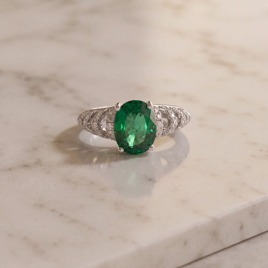 Oval emerald ring in a prong basket with an open pavé diamond band in white gold