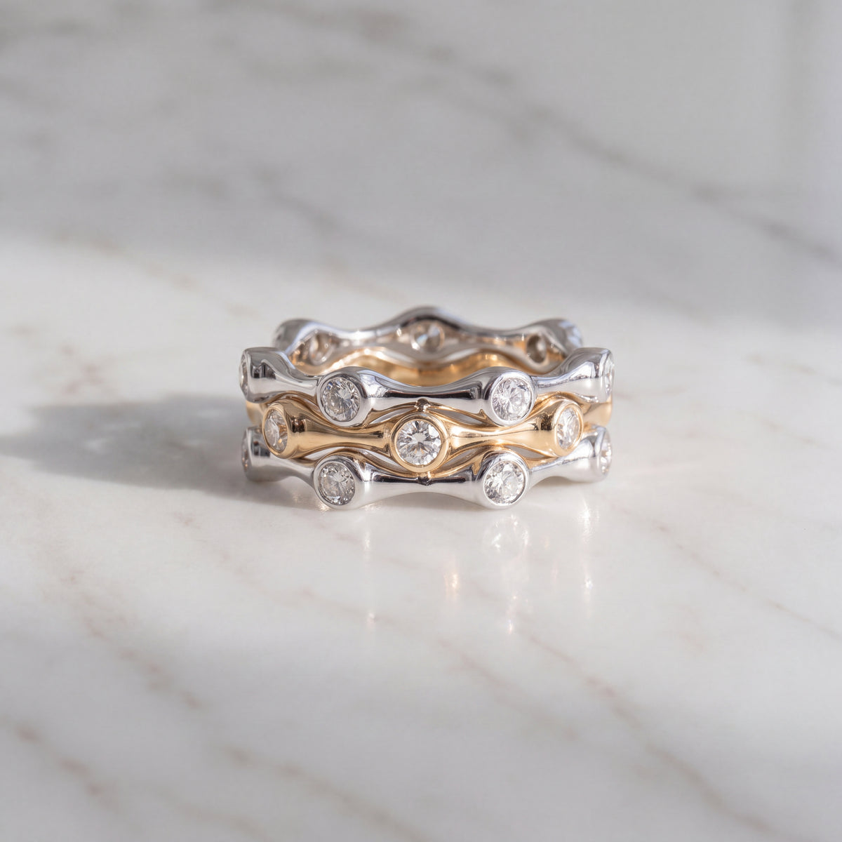 Three wavy stacking rings, white gold on the outside and yellow gold in the middle, with bezel-set round diamonds