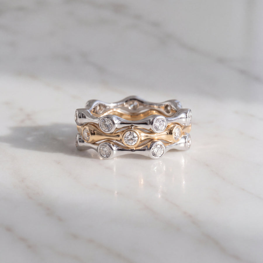 Three wavy stacking rings, white gold on the outside and yellow gold in the middle, with bezel-set round diamonds
