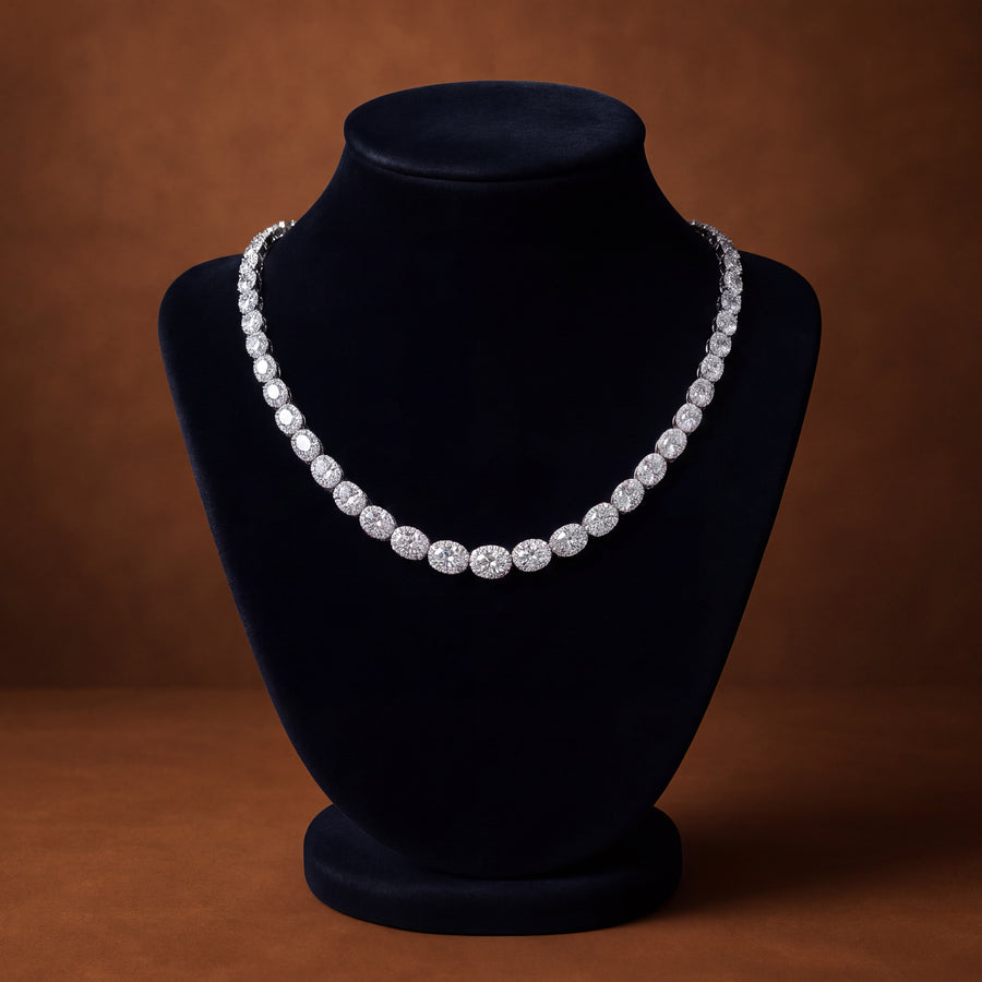 Tennis necklace of oval diamond clusters that graduate in size toward the center, in white gold