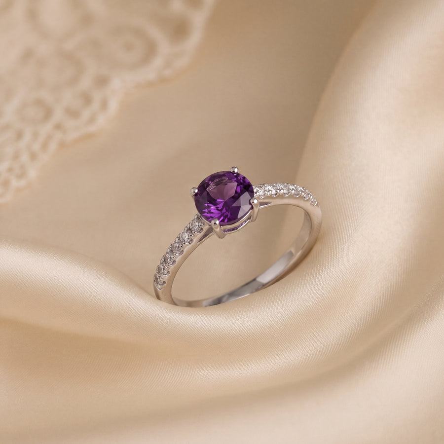 Round amethyst ring in a four-prong setting on a white gold band lined with a row of diamonds