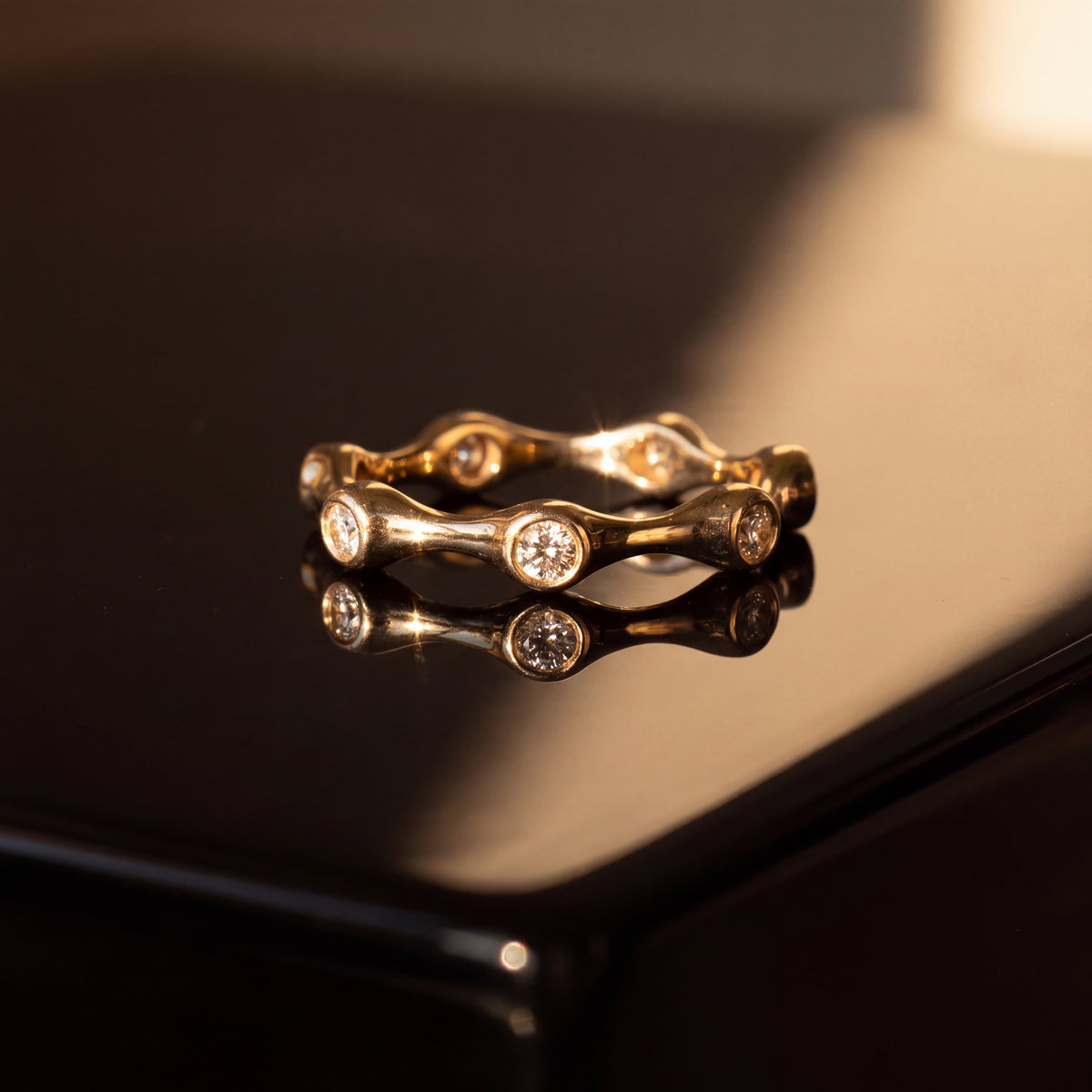 Wavy yellow gold eternity ring with round diamonds bezel set at intervals around the band