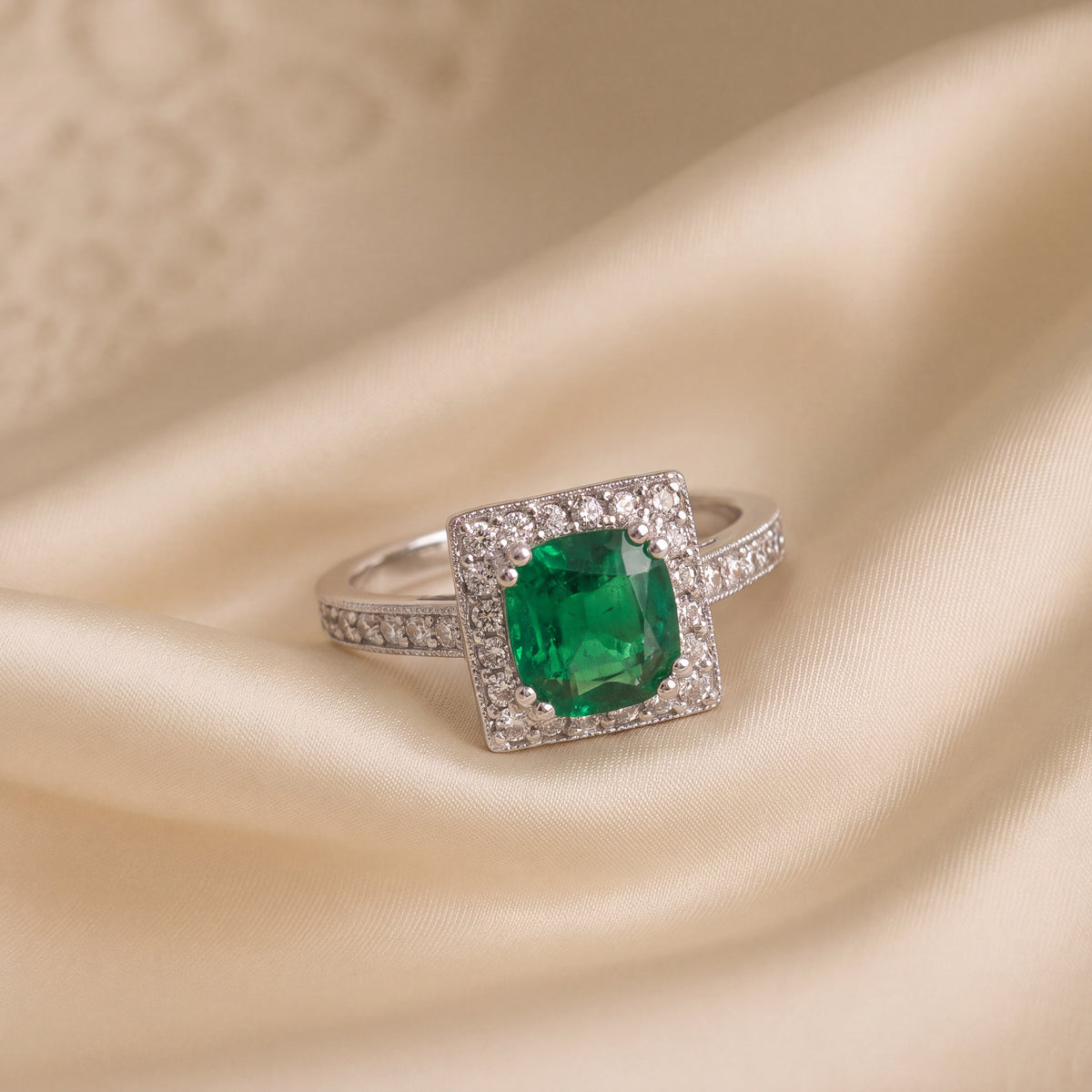 Green emerald in a square diamond halo on a white gold band set with diamonds
