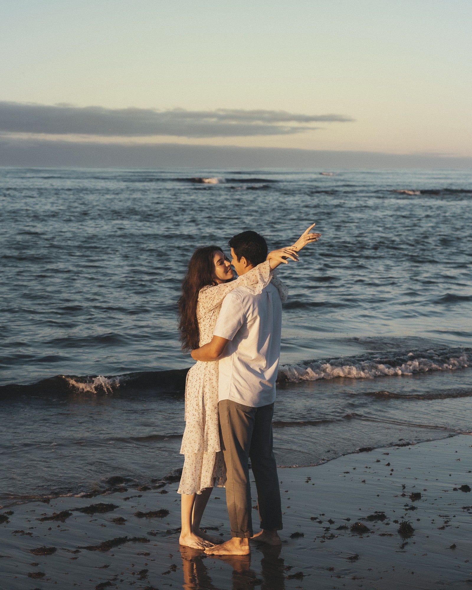 A couple standing barefoot at the waterline