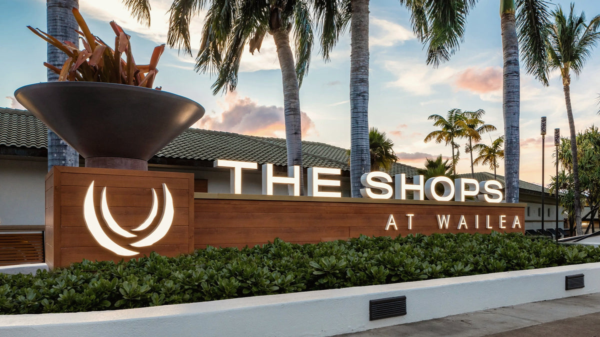 The lit Shops at Wailea entrance sign at sunset, palms behind it