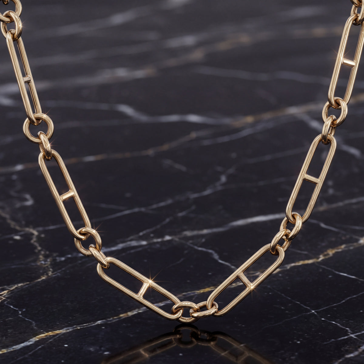 An elongated gold mariner link chain necklace laid out on dark marble.