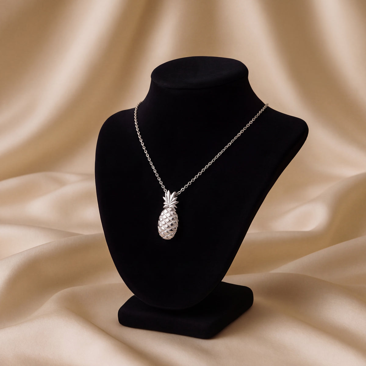 A white gold pineapple pendant with a textured body, on a black bust against gold silk.