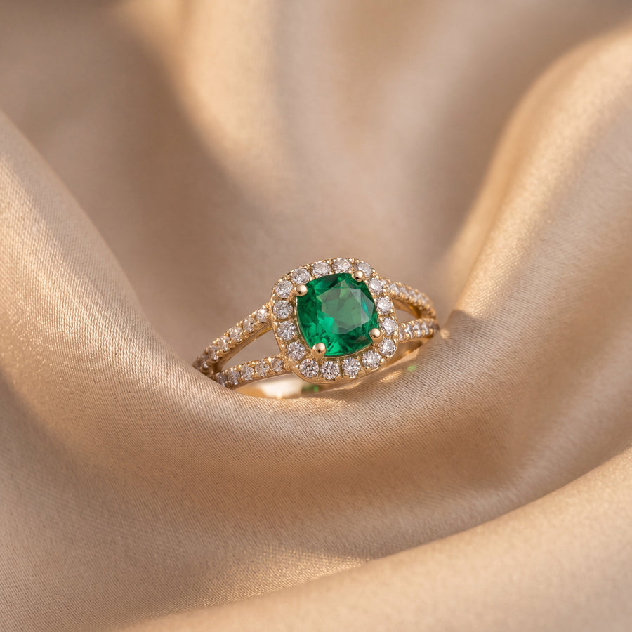 Yellow gold engagement ring with a green emerald in a diamond halo and a pavé diamond split shank