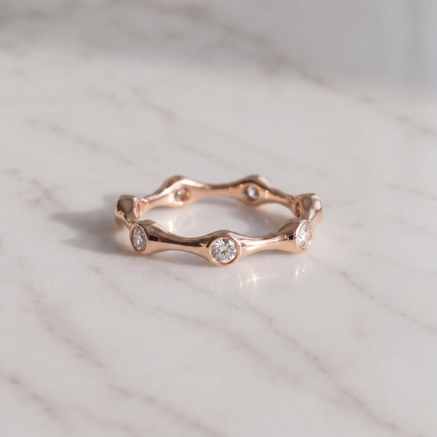 A rose gold eternity ring with a scalloped, wavy edge and bezel-set round diamonds.