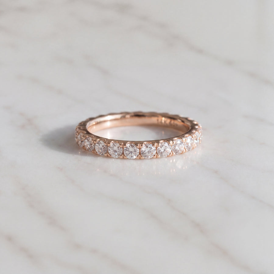 A narrow rose gold eternity ring with small round diamonds in delicate shared prongs.