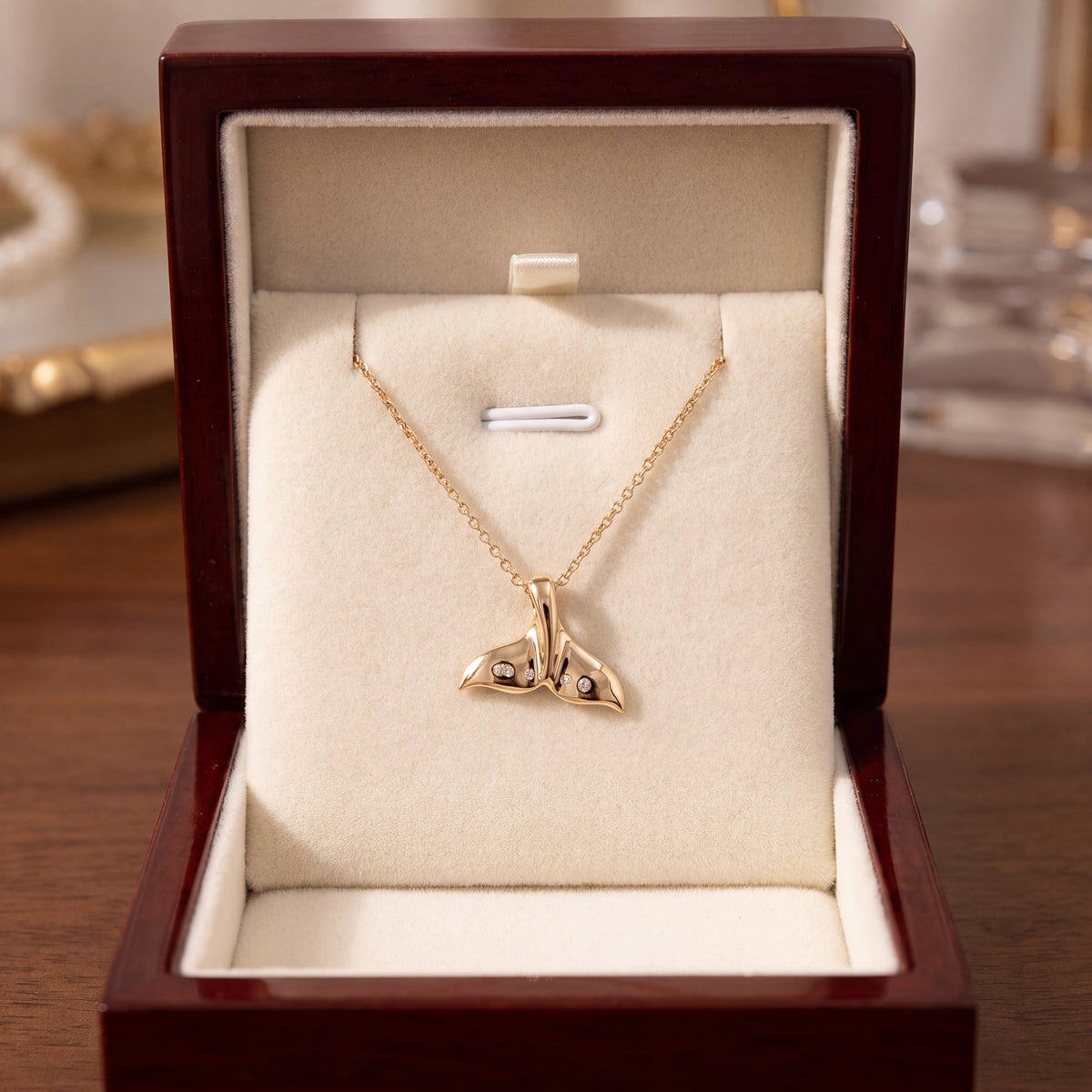 A gold whale tail pendant on a fine chain, in an open wooden presentation box.