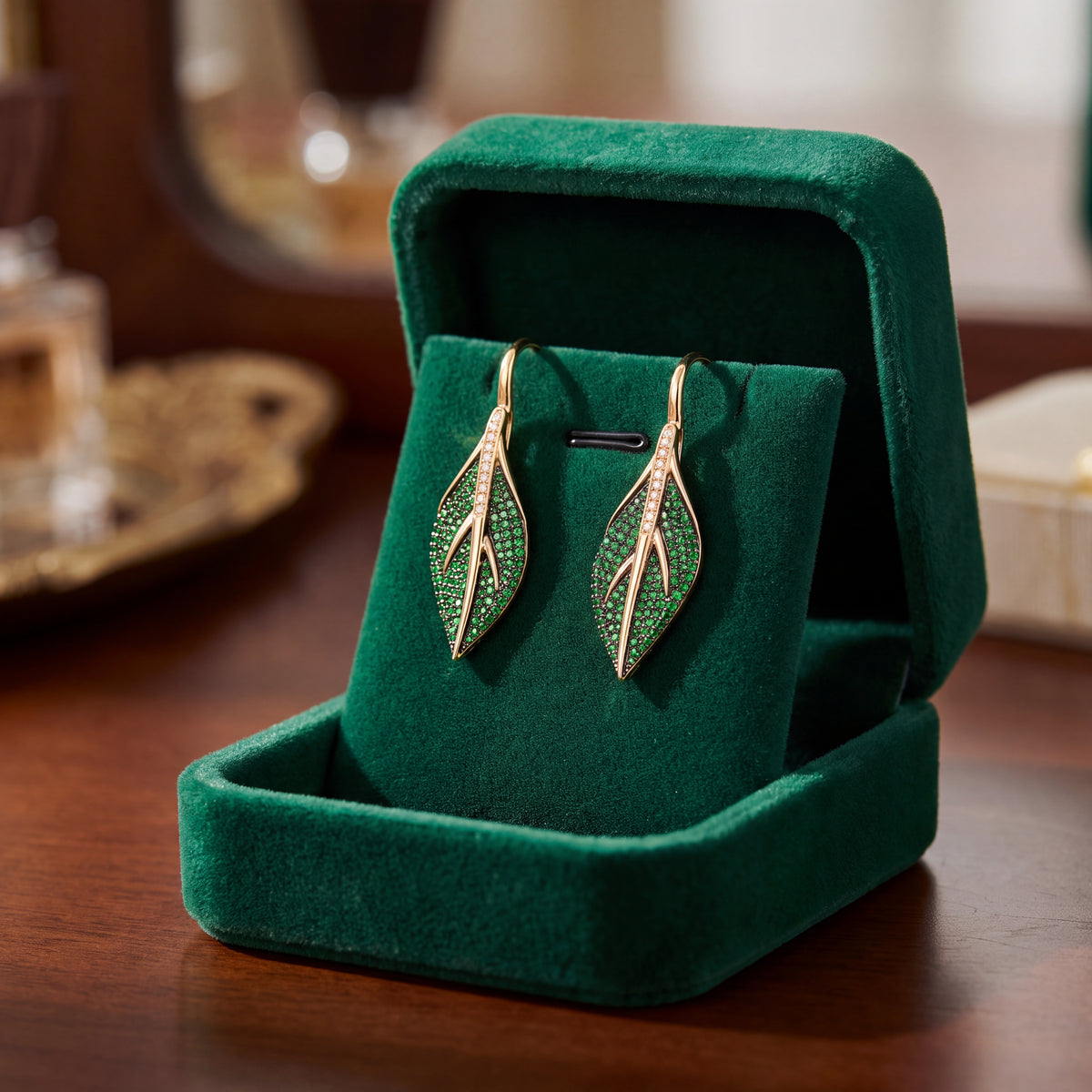 A pair of leaf-shaped drop earrings resting in an open green velvet box.
