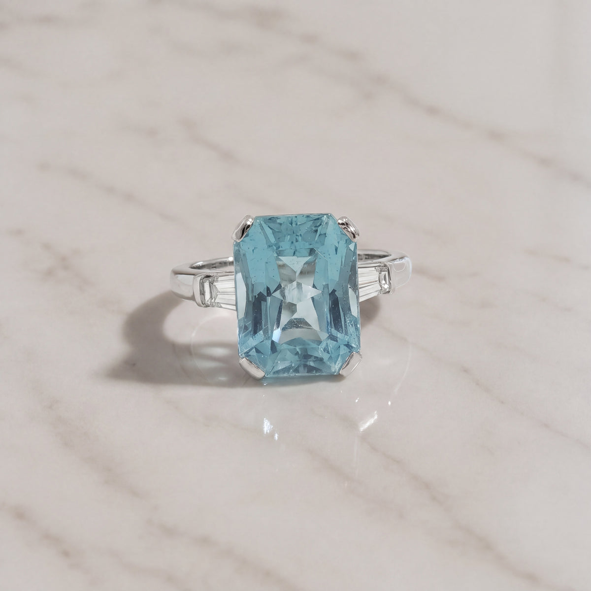 Emerald cut aquamarine ring in four prongs with tapered baguette diamond side stones on a white gold band