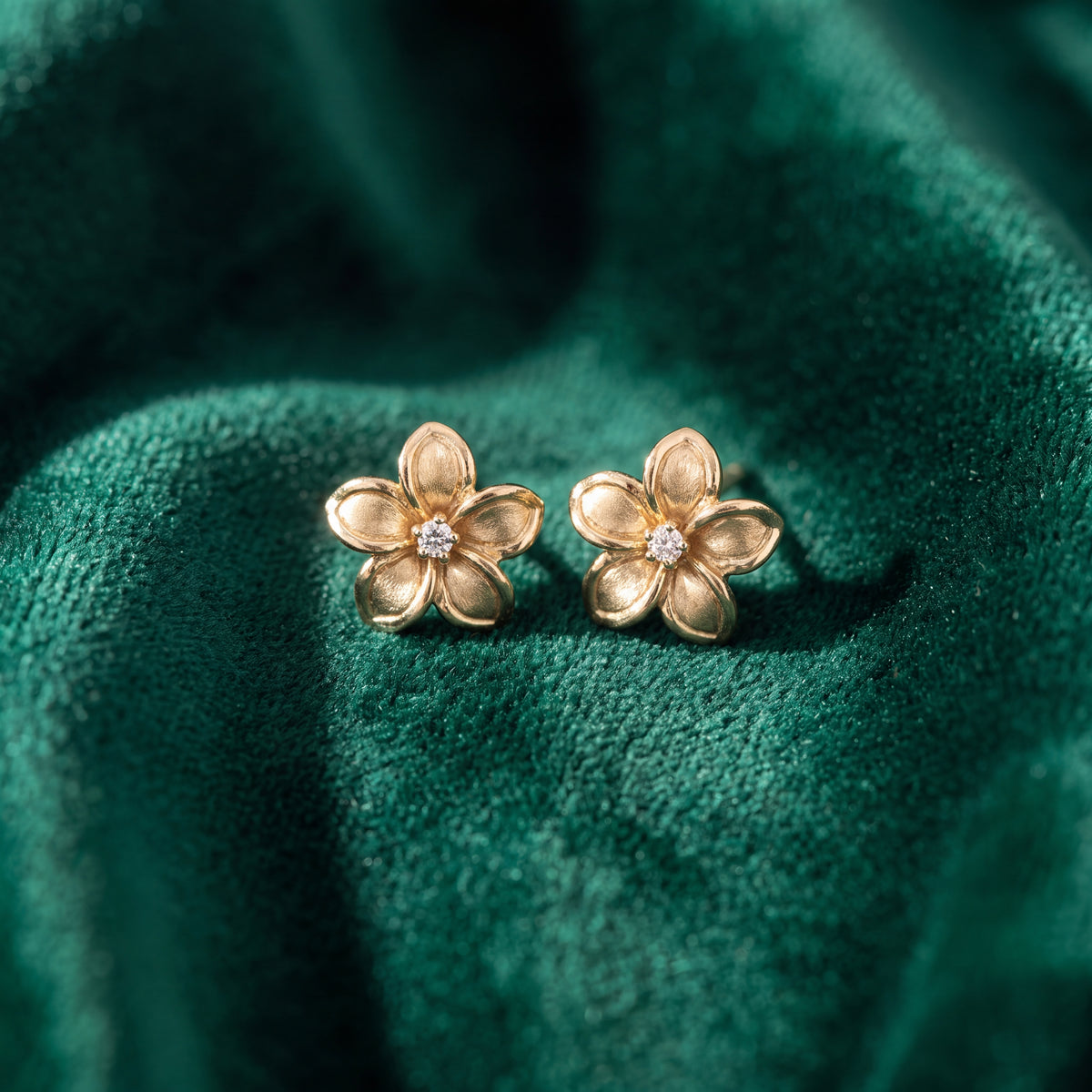 A pair of gold plumeria flower studs with diamond centres, on green velvet.