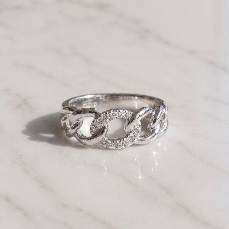 A white gold ring formed of curb chain links, the center link set with pave diamonds.