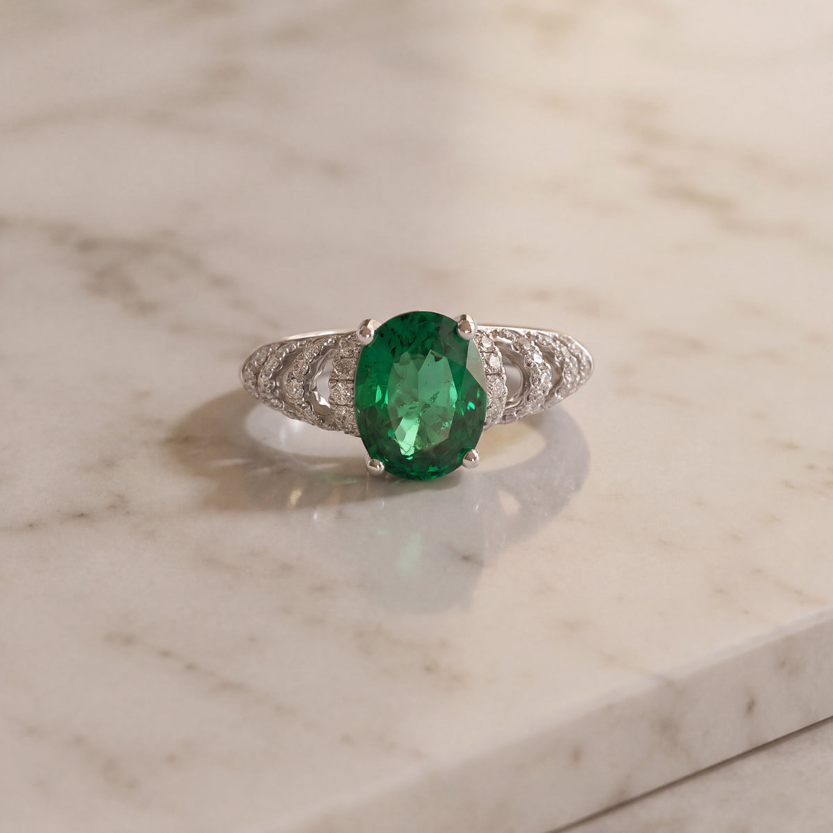 Oval emerald ring in a prong basket with an open pavé diamond band in white gold
