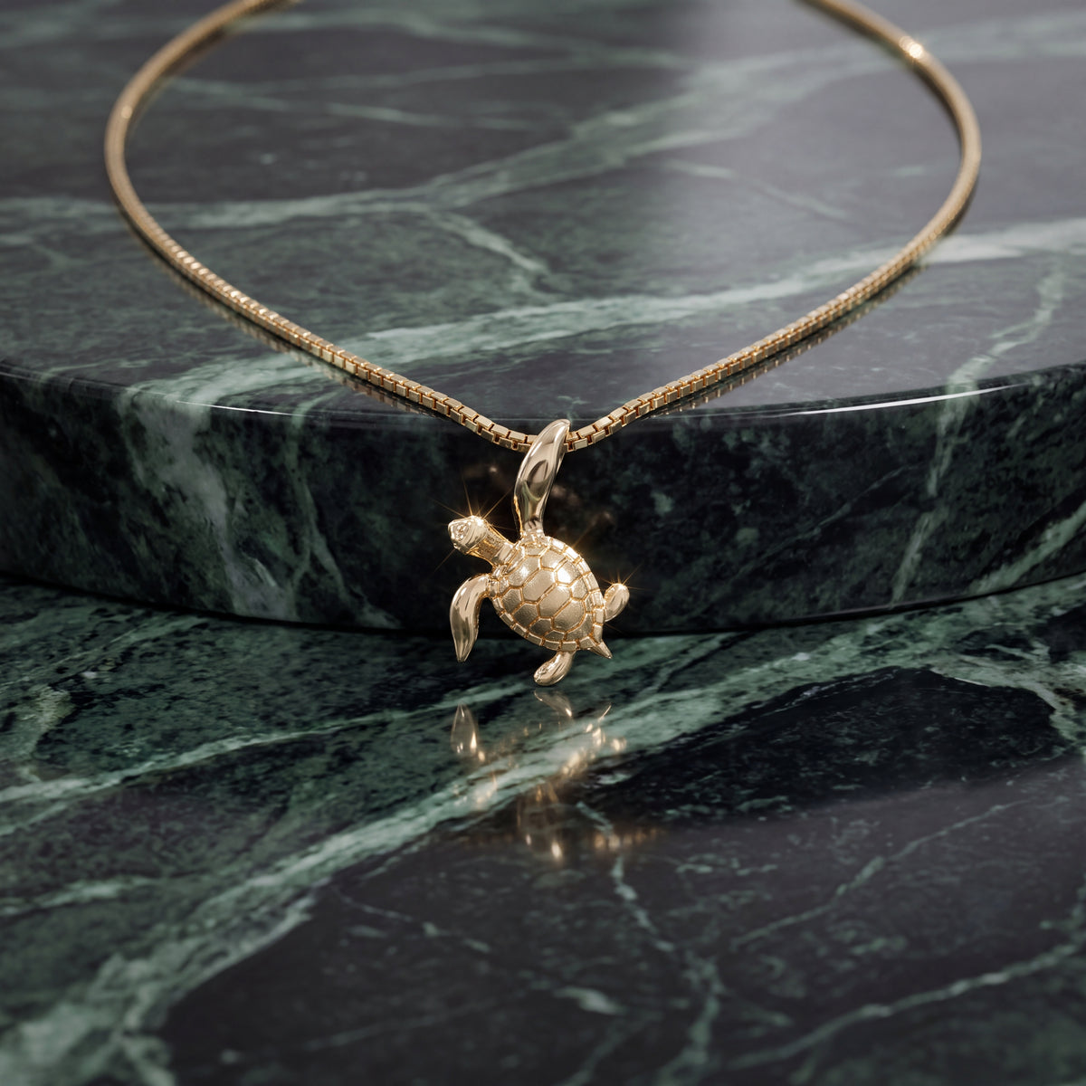 A textured gold sea turtle charm on a fine chain, resting on green marble.