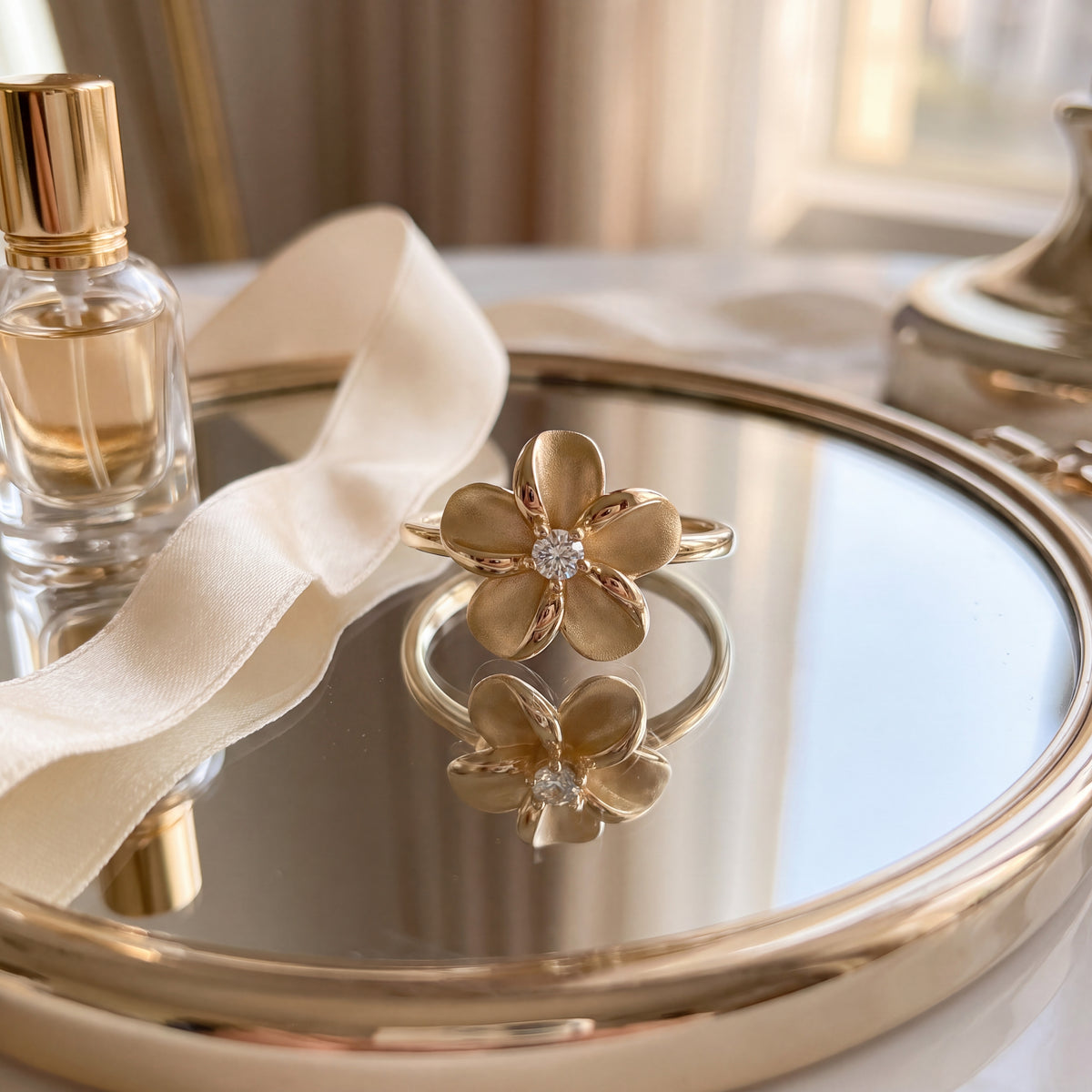 A matte gold plumeria flower ring with a single diamond, on a mirrored tray.