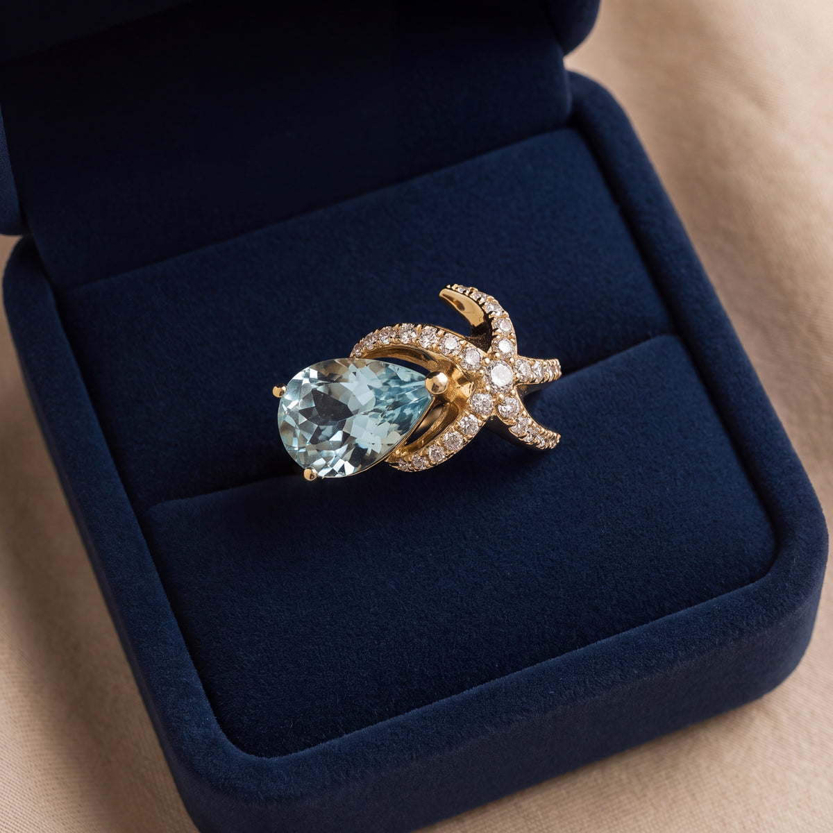 Pear-shaped aquamarine cocktail ring in yellow gold with a diamond-set starfish wrapping around the center stone
