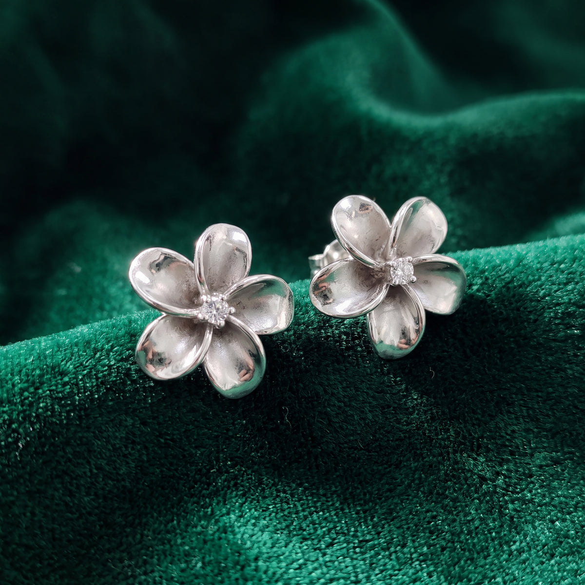 A pair of white gold plumeria flower studs with diamond centres, on green velvet.