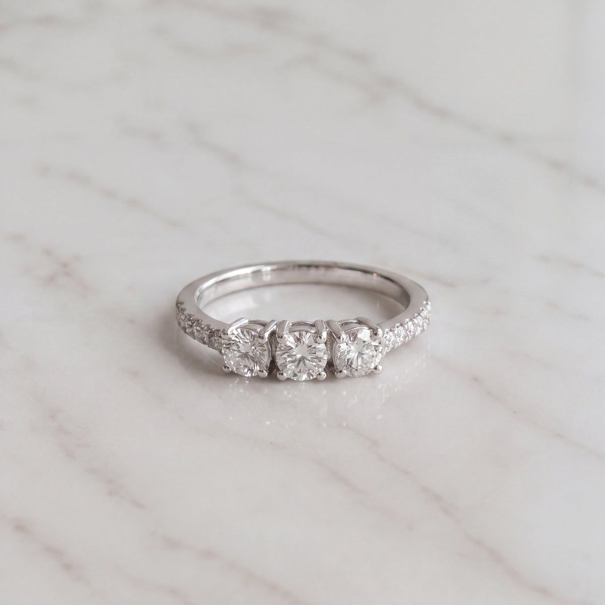 Three round diamonds on a white gold band with pave diamonds along the shoulders.