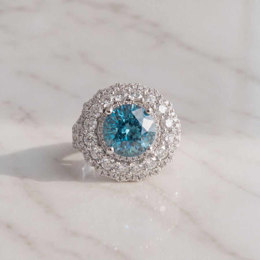 Round blue center stone in a double diamond halo on a white gold cocktail ring