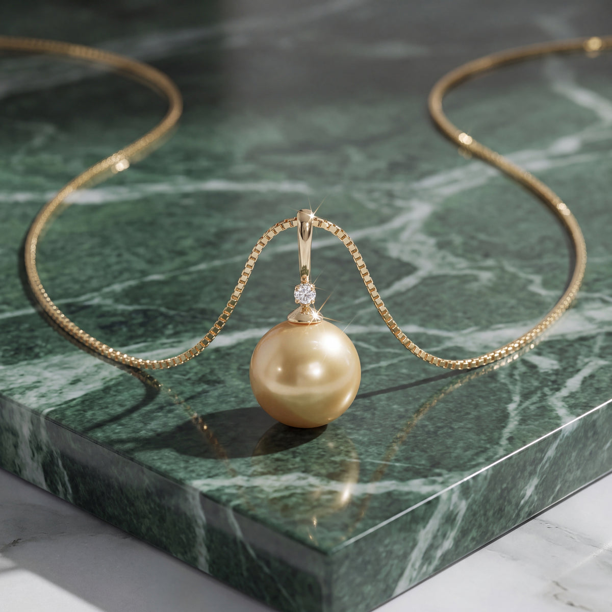 A golden pearl in a diamond-set cap, hanging from a fine gold chain over green marble.