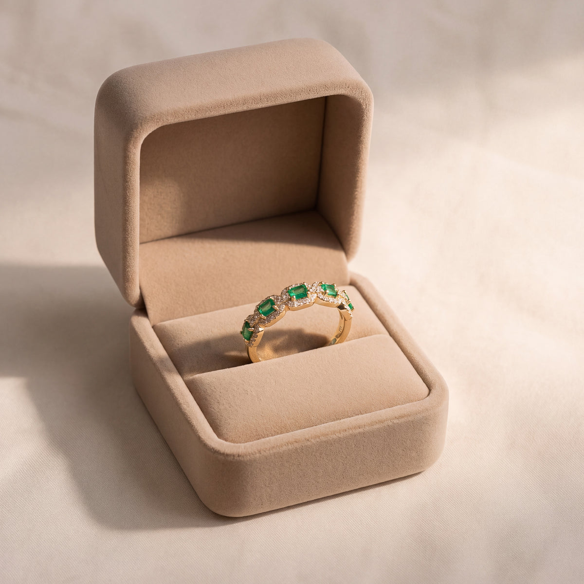 Yellow gold band of baguette emeralds, each framed by a halo of small diamonds, linked in a scalloped row