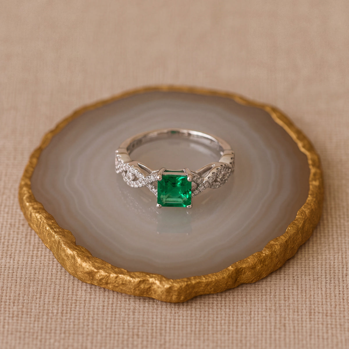 Emerald-cut emerald in four prongs on a white gold interwoven twisted band set with small diamonds