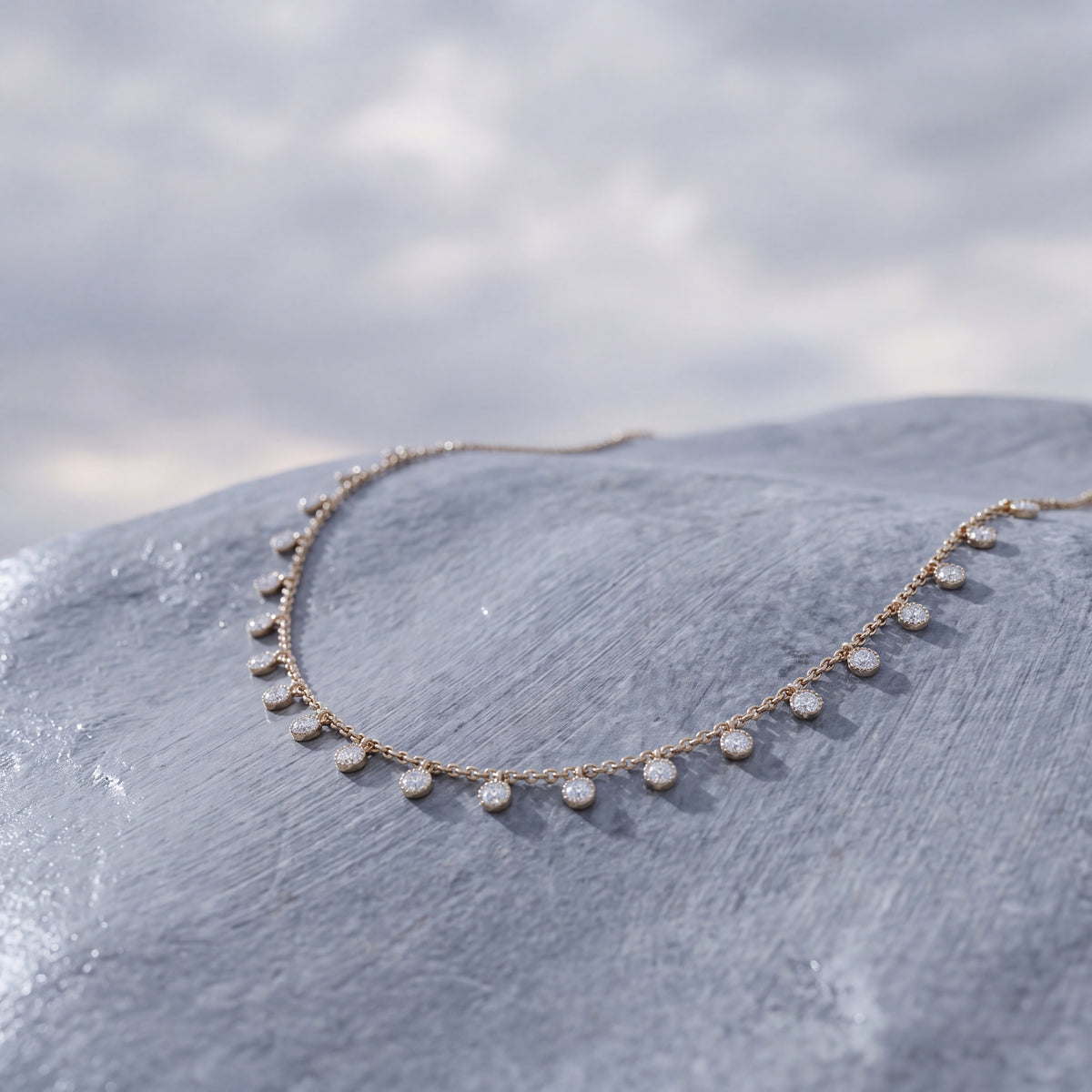 A fine gold chain hung with a row of small diamond discs, against a pale sky.
