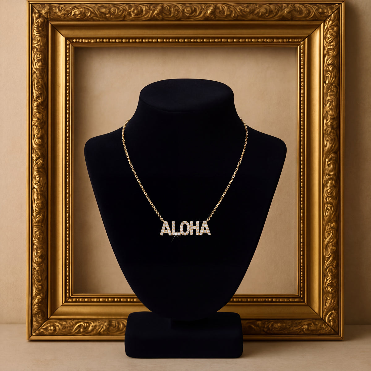 The word ALOHA in diamond-set gold block letters, on a navy bust inside a gilt frame.