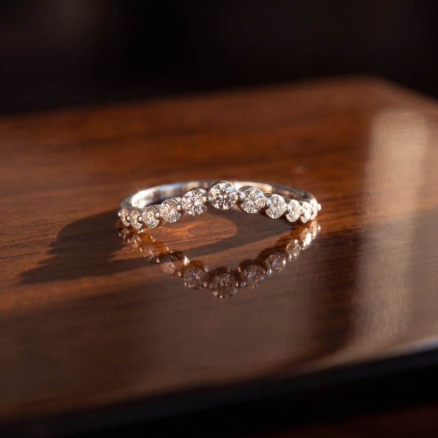 Curved white gold wedding band with a row of round diamonds in shared prong settings