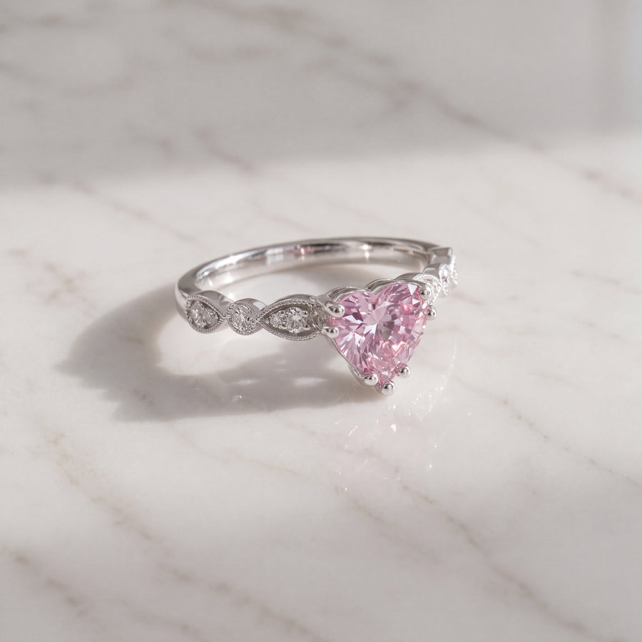 Heart-cut pink sapphire ring in prongs on a 14K white gold band with diamond accents and milgrain