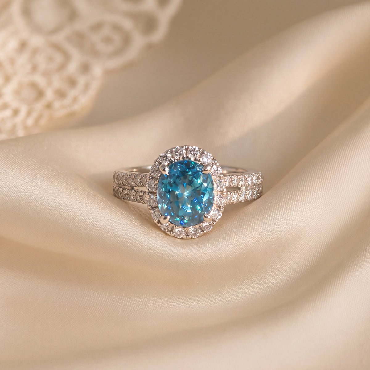 Oval blue zircon cocktail ring in a round diamond halo on a white gold split shank band with pavé diamonds