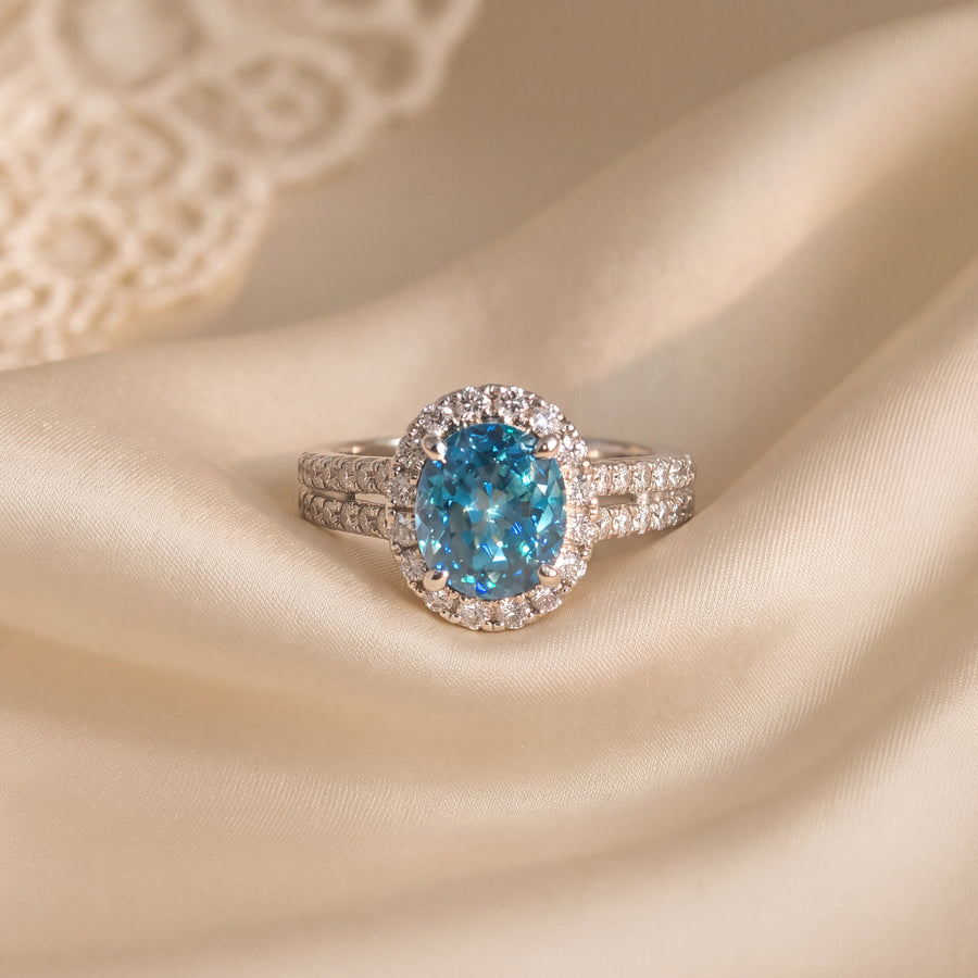 Oval blue zircon cocktail ring in a round diamond halo on a white gold split shank band with pavé diamonds