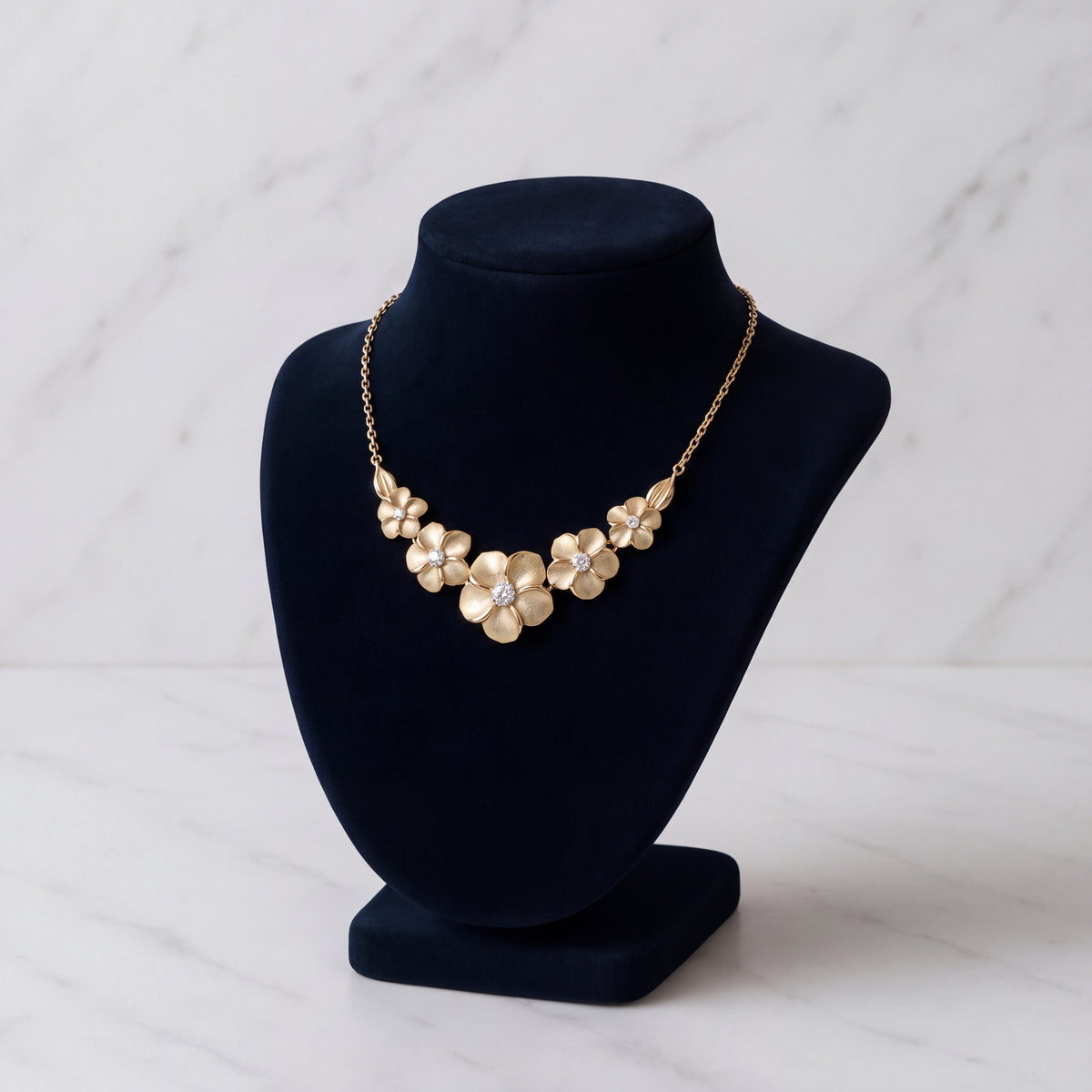 A row of gold plumeria flowers along a fine chain, on a black velvet bust.