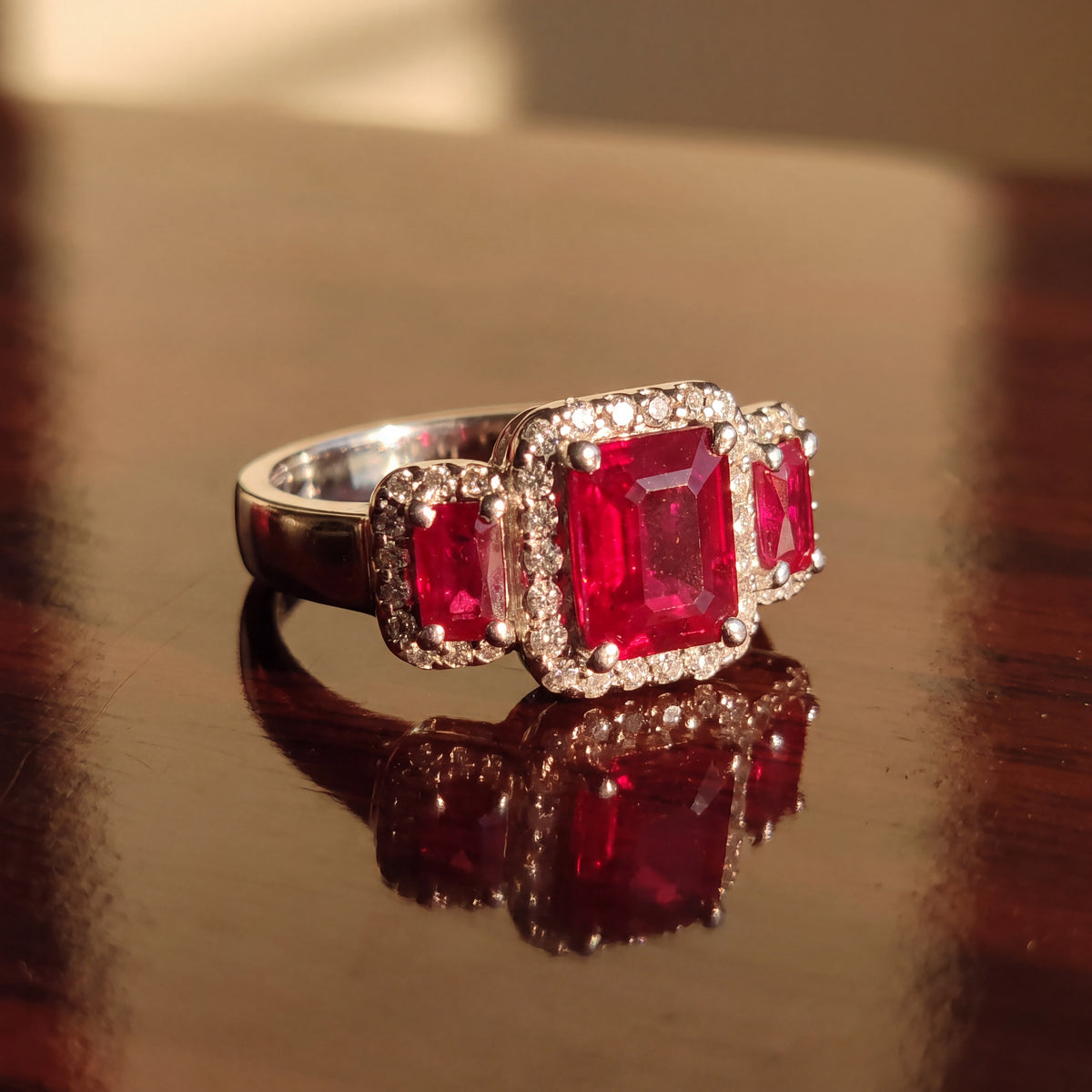 Three emerald-cut rubies, each in a diamond halo, on a white gold band