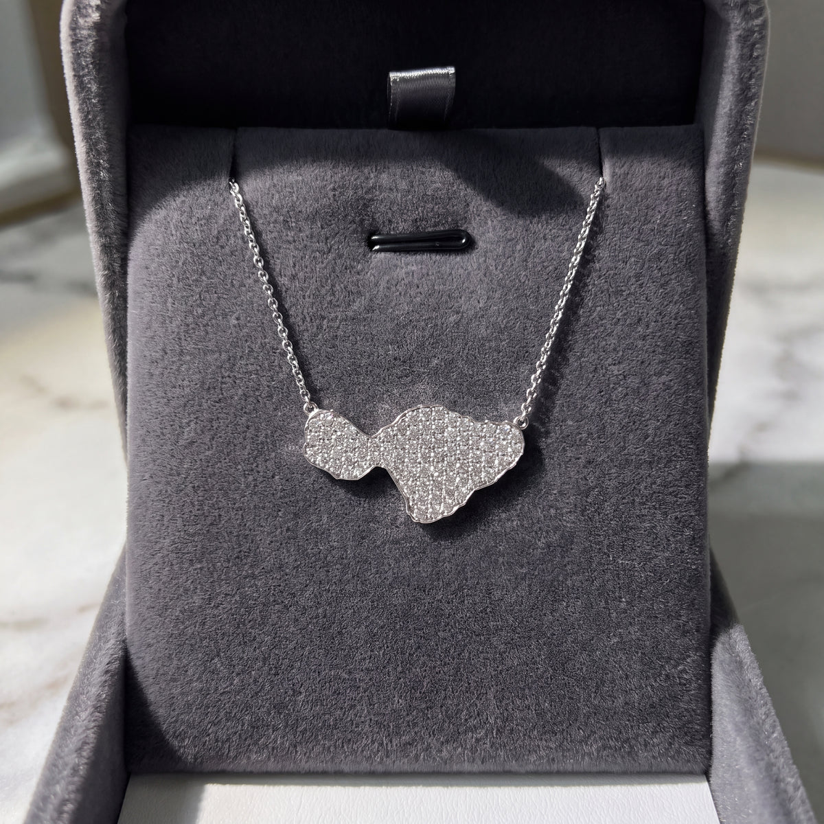 A diamond-paved island silhouette on a fine white gold chain, in an open grey box.