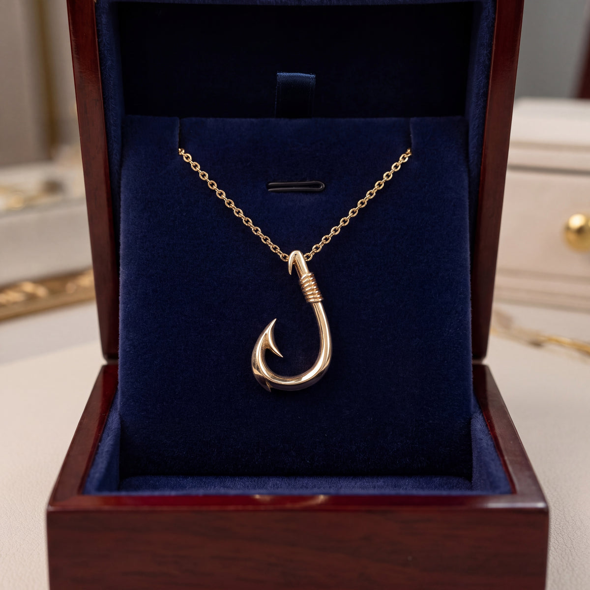 A smooth gold fish hook pendant on a fine chain, in an open navy velvet box.