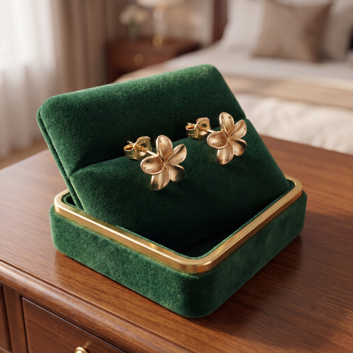 A pair of gold flower stud earrings resting in an open green velvet box on a wooden chest.