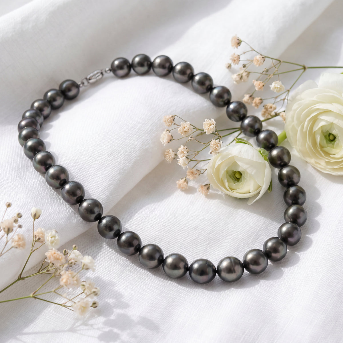 A knotted strand of dark grey pearls laid among white flowers.