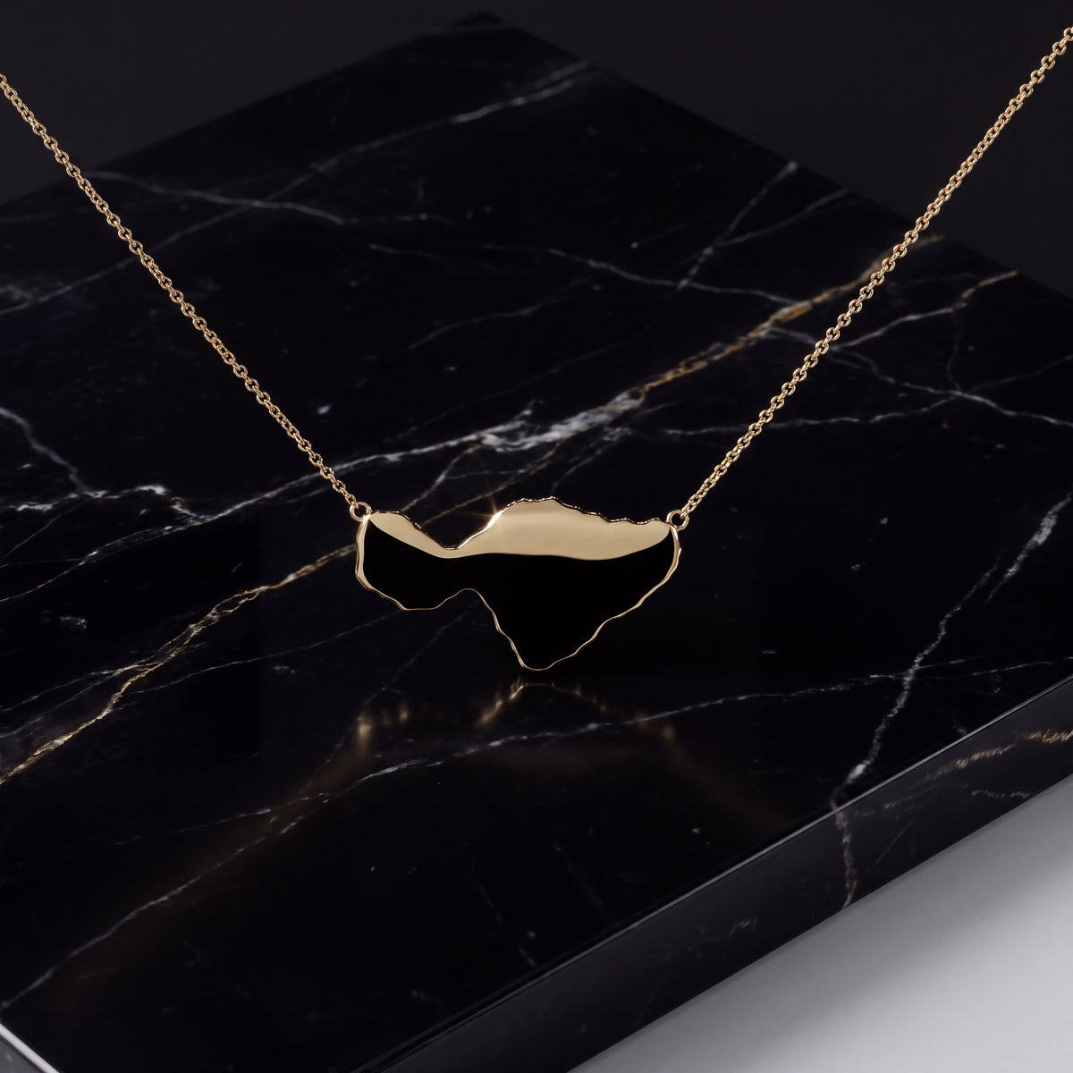A polished gold island silhouette on a fine chain, laid on black marble.