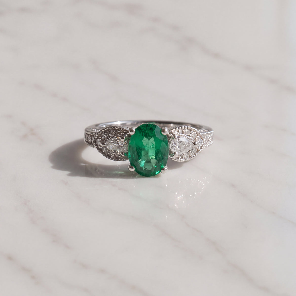 Oval emerald ring flanked by pear-shaped diamonds with milgrain detail in white gold