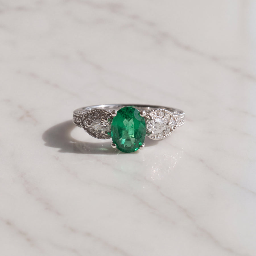 Oval emerald ring flanked by pear-shaped diamonds with milgrain detail in white gold