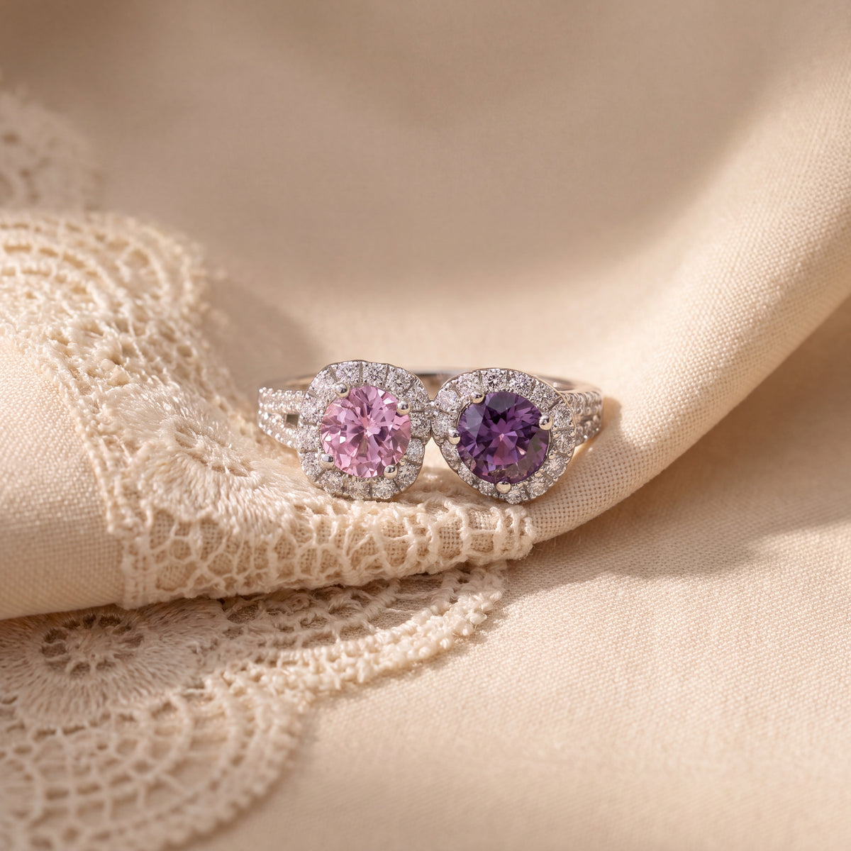 White gold ring with a pink and a purple round sapphire side by side, each in a diamond halo, on a diamond band