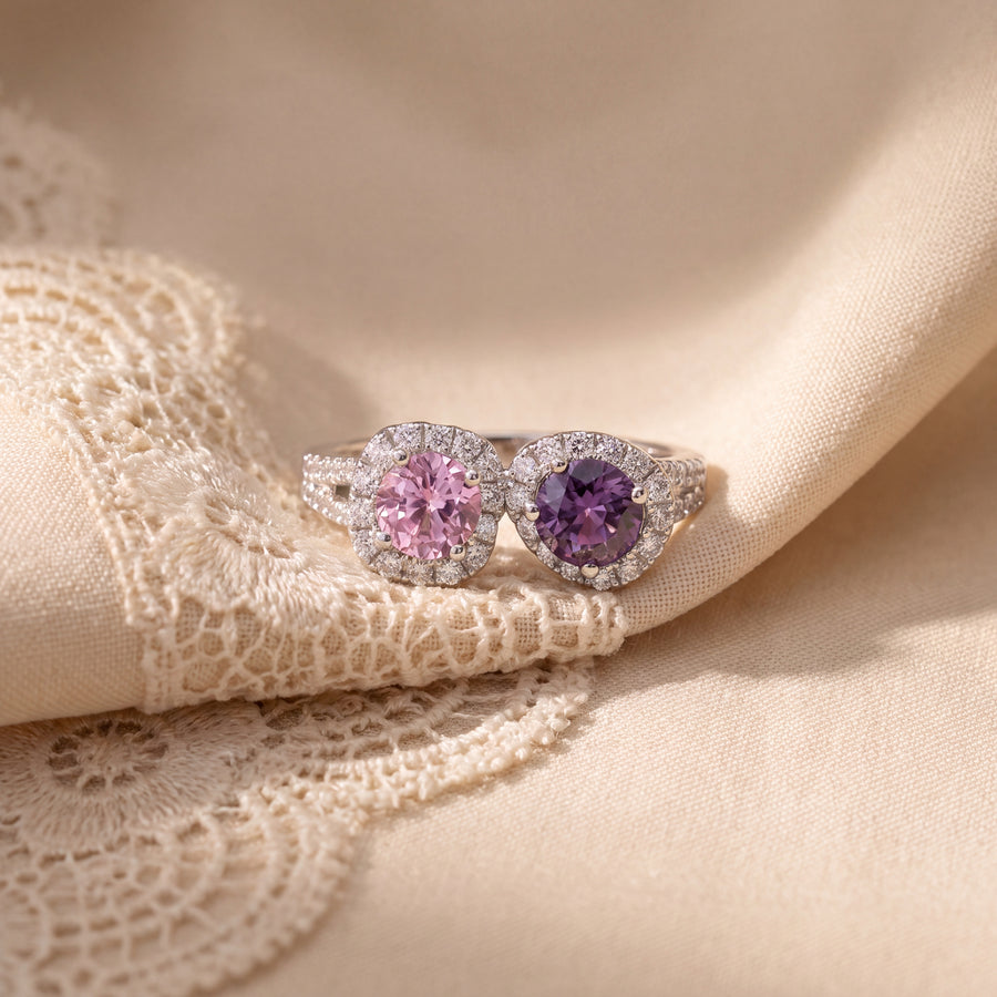 White gold ring with a pink and a purple round sapphire side by side, each in a diamond halo, on a diamond band